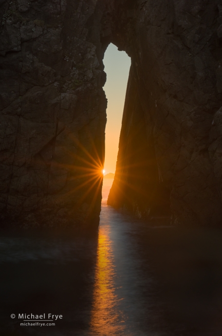 Sun setting through a natural bridge, Oregon coast, USA